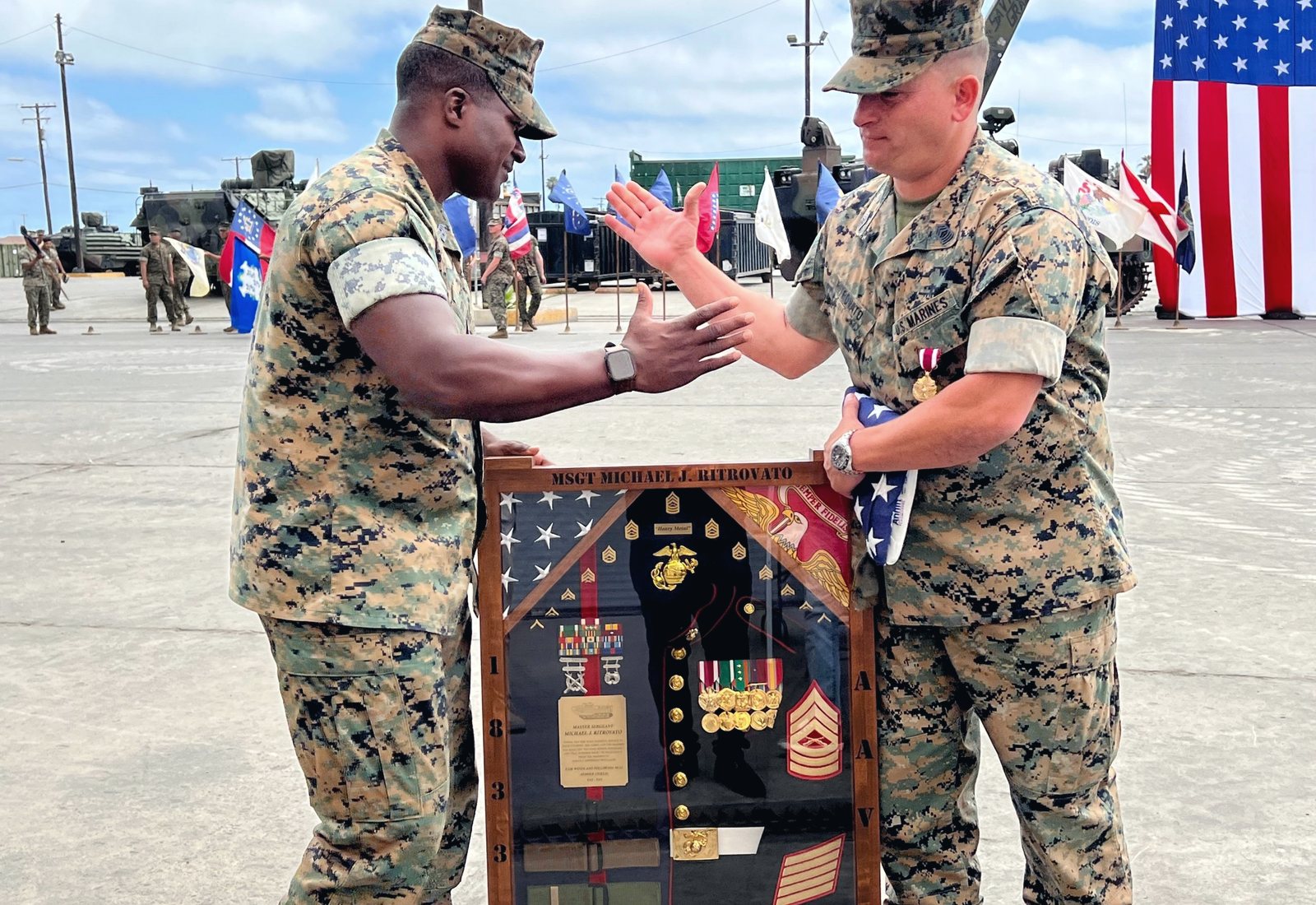Mike Ritrovato in MARPAT utilities at his retirement ceremony, holding a folded flag beside a shadow box engraved MSGT Michael J. Ritrovato